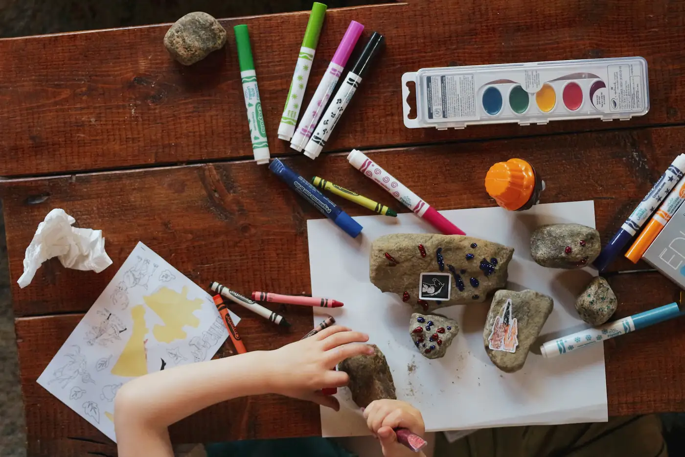 Children's hands with markers and painted rocks on a table