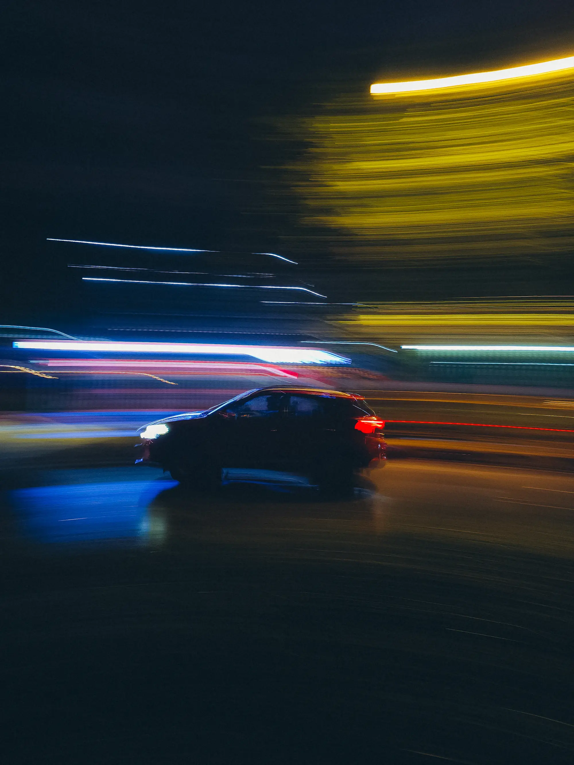A dark car moving fast at night through streaks of city light