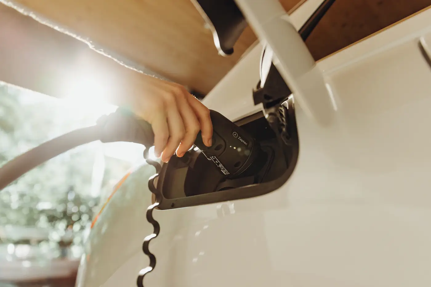 A hand plugging a charging cable into a white car