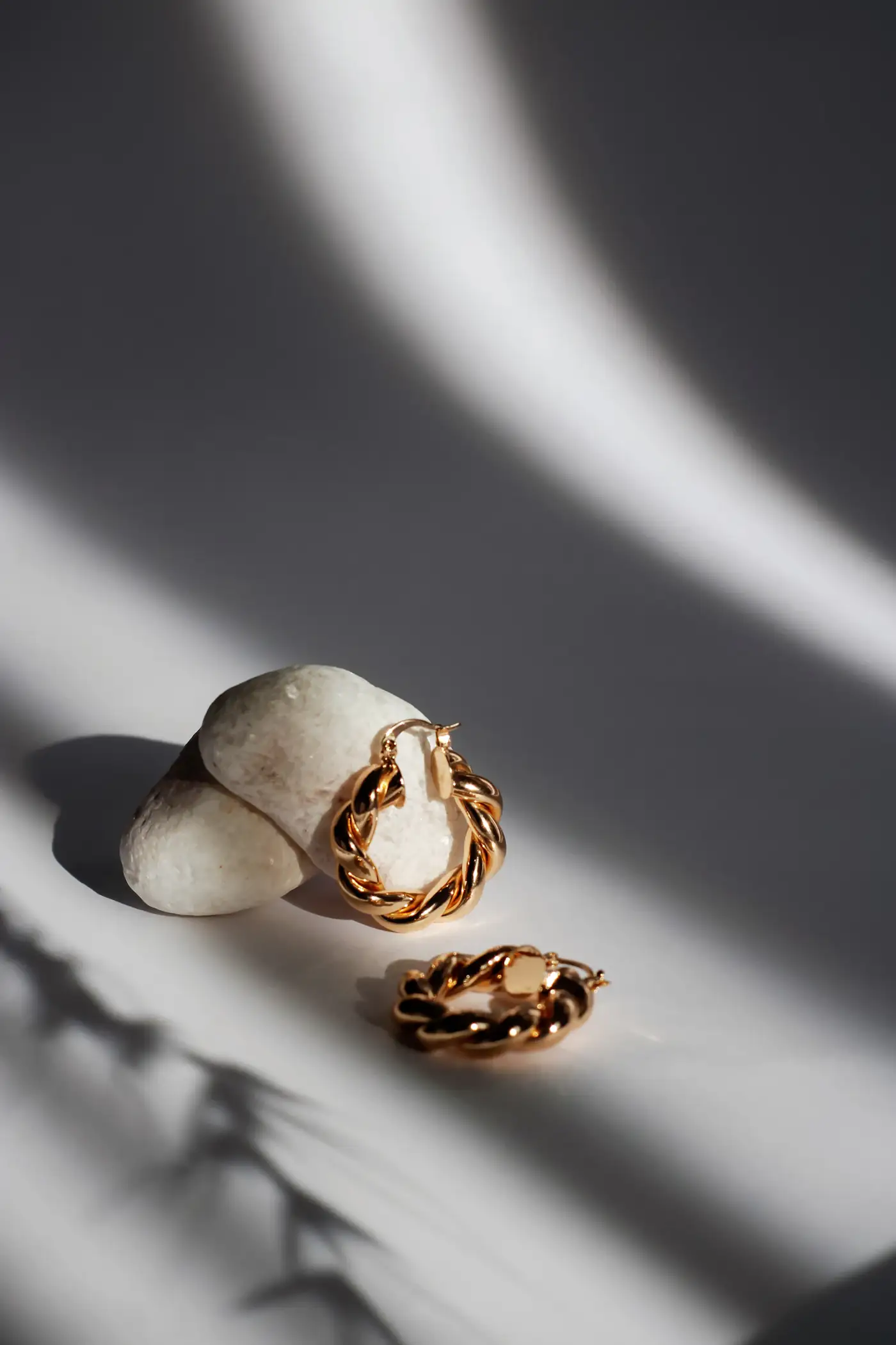 Gold chain hoops on a white stone with hard shadows