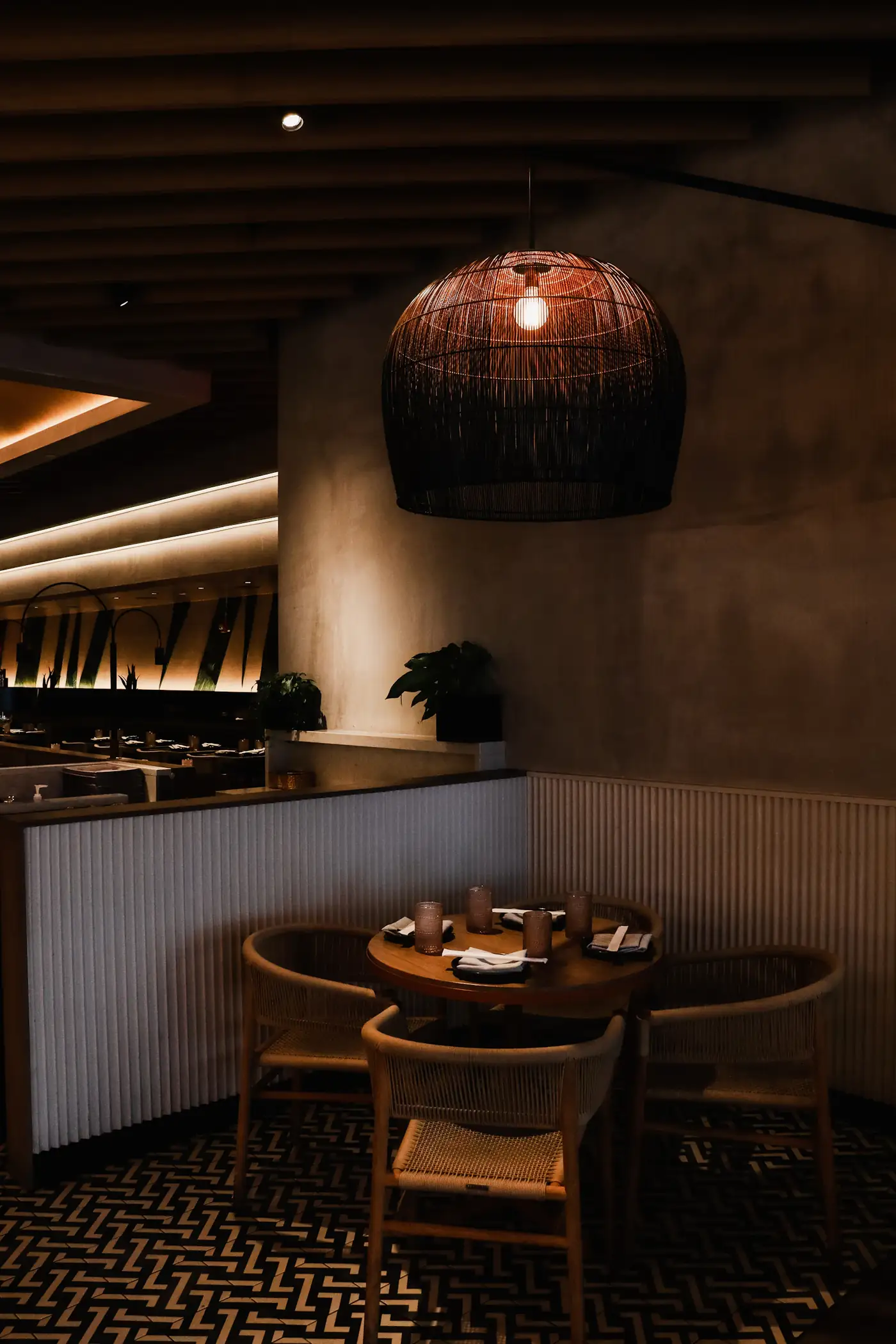 Dark dining room with a woven lamp and banquettes