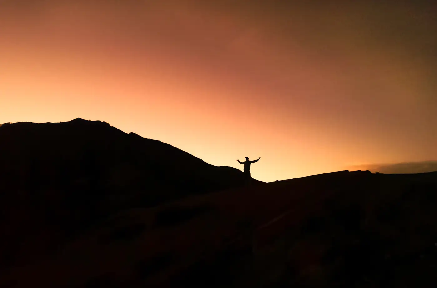 Silhouette of a person standing on a ridge at sunset